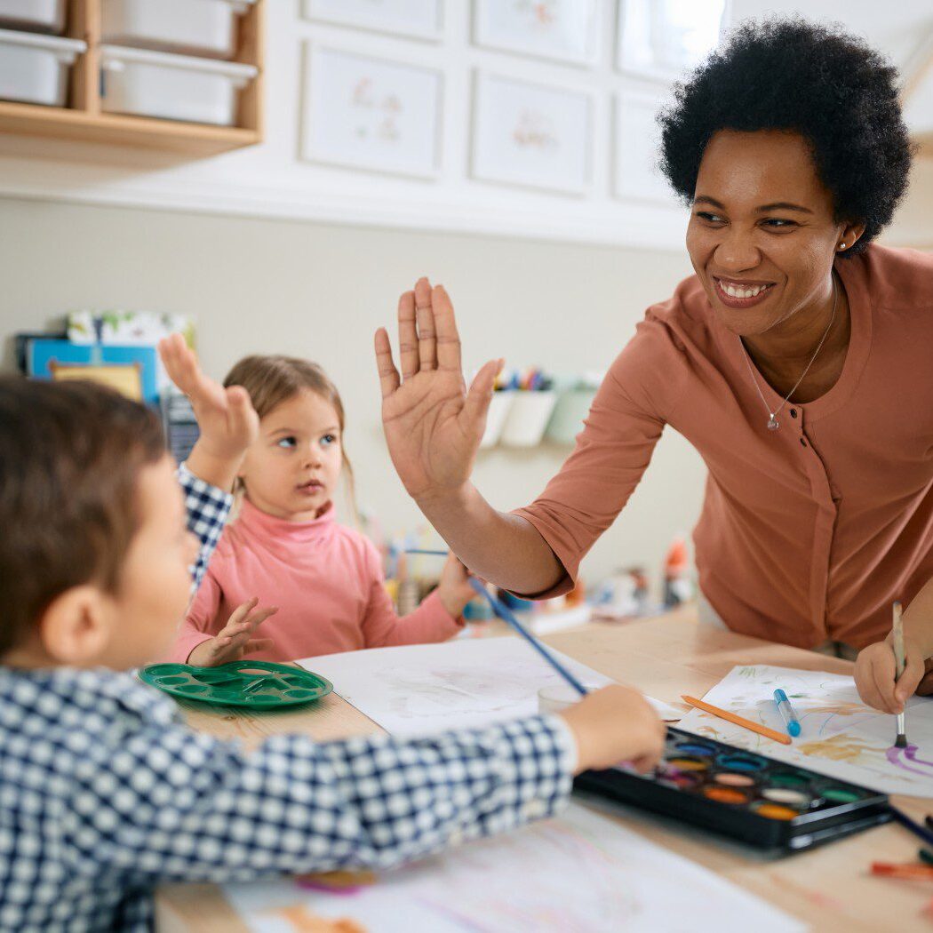 Teacher high-fives children in classroom activity.